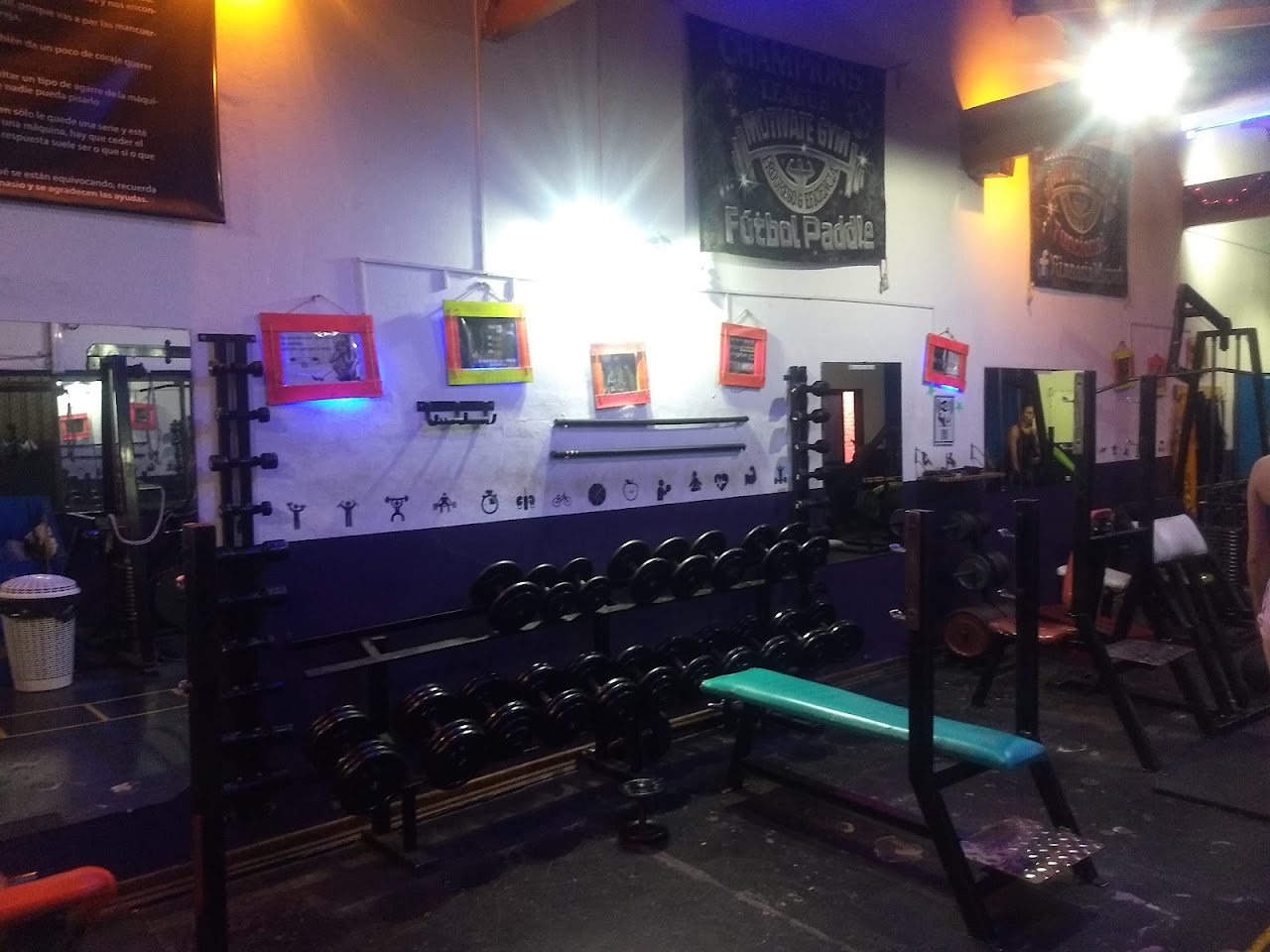 Área de fuerza y racks con iluminación perimetral dorada y equipamiento profesional